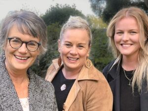 Head-and-shoulders photo of three collaborators smiling at the camera outdoors — writer, designer, and marketer — representing the creative team behind the Branding Kickstart Collaboration.